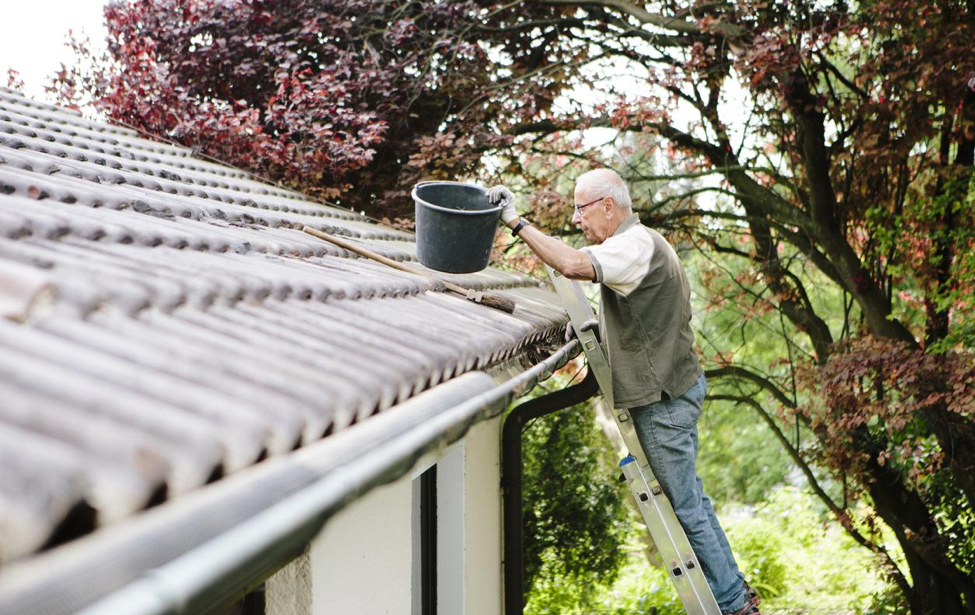 Man cleaning roof gutters with a bucket.